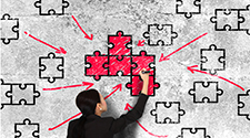 Image of a woman drawing on a board showing many puzzle pieces coming together with directional arrows